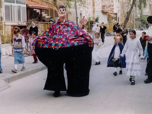 Children dressed in costume and carrying mishloach manot follow a costumed clown on Purim day in Jerusalem, Israel. (Wikimedia Commons)