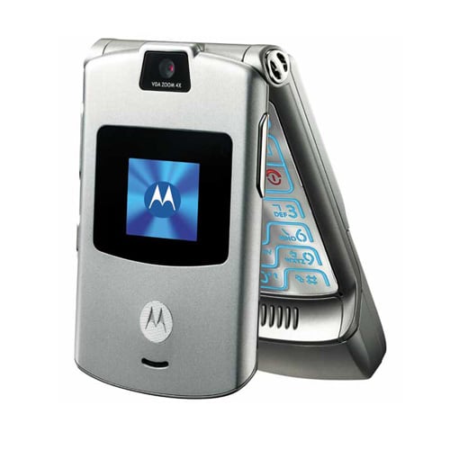 A silver Motorola flip phone is partially open, showing a small external screen with the Motorola logo. The phones keypad is visible, illuminated with blue backlighting. The device has a camera near the hinge.