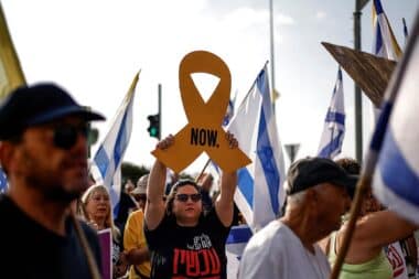 An Israeli woman raises a cutout of a yellow ribbon as others wave Israeli flags, during an anti-government protest demanding a deal to release Israeli hostages held in the Gaza Strip by Hamas terrorists since October 7, 2023, near the northern town Kiryat Shmona on August 17, 2025.