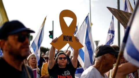 An Israeli woman raises a cutout of a yellow ribbon as others wave Israeli flags, during an anti-government protest demanding a deal to release Israeli hostages held in the Gaza Strip by Hamas terrorists since October 7, 2023, near the northern town Kiryat Shmona on August 17, 2025.
