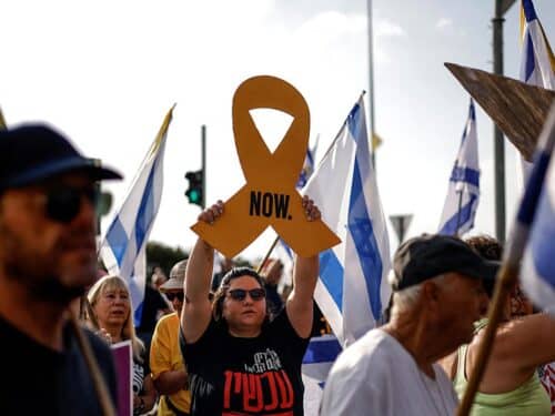An Israeli woman raises a cutout of a yellow ribbon as others wave Israeli flags, during an anti-government protest demanding a deal to release Israeli hostages held in the Gaza Strip by Hamas terrorists since October 7, 2023, near the northern town Kiryat Shmona on August 17, 2025.
