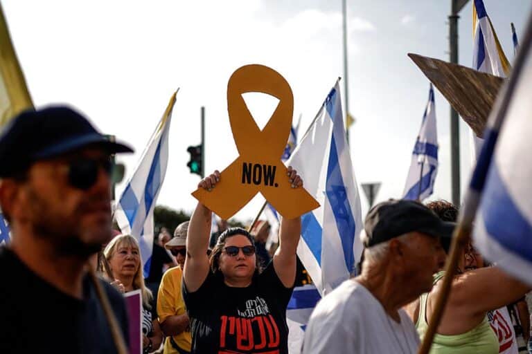 An Israeli woman raises a cutout of a yellow ribbon as others wave Israeli flags, during an anti-government protest demanding a deal to release Israeli hostages held in the Gaza Strip by Hamas terrorists since October 7, 2023, near the northern town Kiryat Shmona on August 17, 2025.