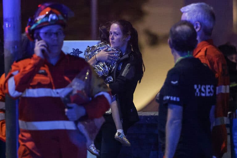 A woman holds a child in a blanket after a shooting incident at Bondi Beach in Sydney on December 14, 2025. Australian police said two people were in custody following reports of multiple gunshots on December 14 at Sydney's famed Bondi Beach, urging the public to take shelter. (Photo by DAVID GRAY / AFP via Getty Images)