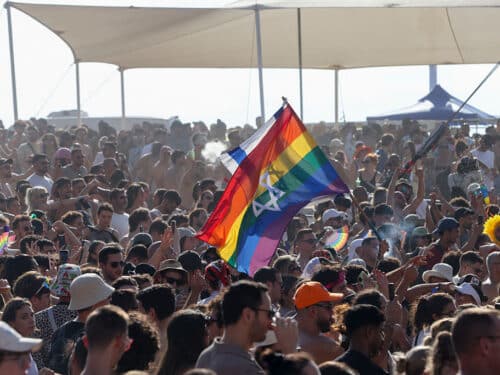 A participant waves an Israeli flag and a rainbow flag with a Star of David above a crowd during the annual Pride Parade in Tel Aviv, Israel, on June 12, 2026. The event marks the 28th edition of the parade and the first since the October 7 attacks. Recognized as the largest Pride march in the Middle East, the gathering in the Israeli coastal metropolis was expected to draw around 150,000 people. (Photo by Simon Beni / Middle East Images / AFP via Getty Images)